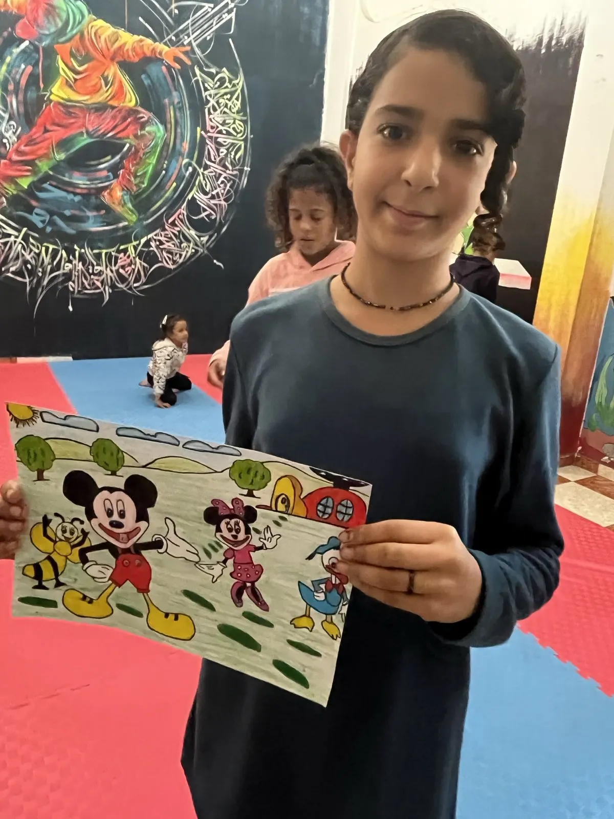 Girl proudly showing her colorful cartoon drawing at the Colors of Hope workshop